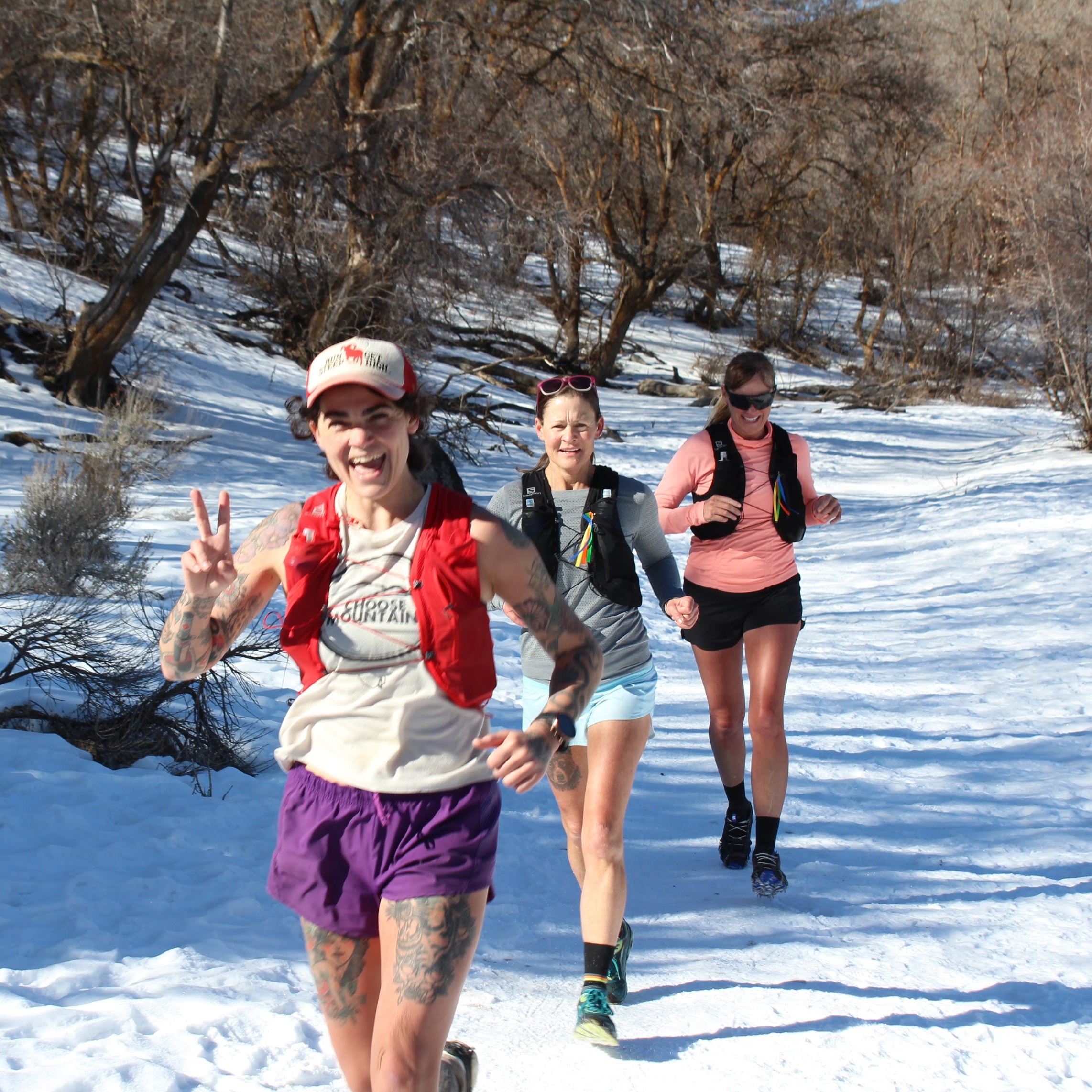 Three trail runners heading up a snowy trail in the mountains.